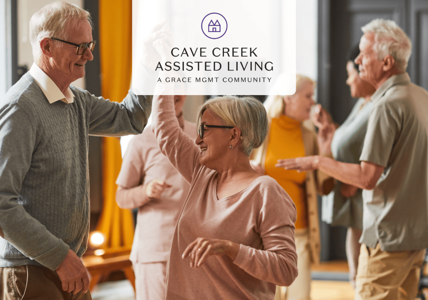 Seniors dancing and smiling in a community room under a logo banner that reads Cave Creek Assisted Living.